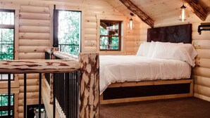 A log cabin bedroom with a bed, a table, and a view of the outdoors. - Incredible Treehouse with Treetop Views - Sleeps up to 6 (Millersburg)
