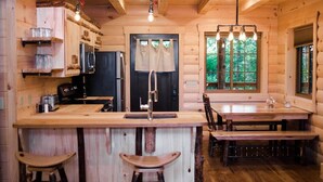 A wooden cabin interior with a kitchen, dining area, and bar stools. - Incredible Treehouse with Treetop Views - Sleeps up to 6 (Millersburg)