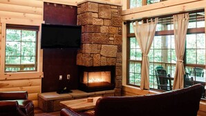 A cozy cabin interior with a stone fireplace, wooden walls, and large windows. - Incredible Treehouse with Treetop Views - Sleeps up to 6 (Millersburg)