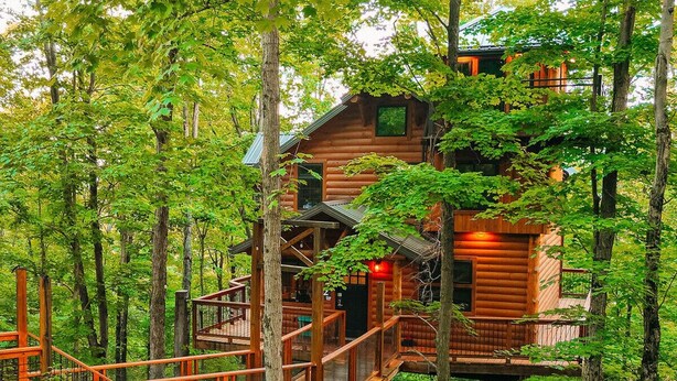 A wooden cabin elevated among trees with a wooden deck and stairs. - Incredible Treehouse with Treetop Views - Sleeps up to 6 (Millersburg)