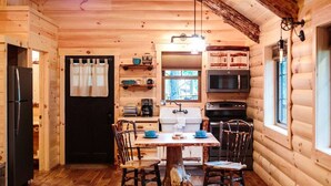 Een houten cabin met een eettafel, stoelen, een koelkast, een fornuis, een magnetron en een gootsteen.
