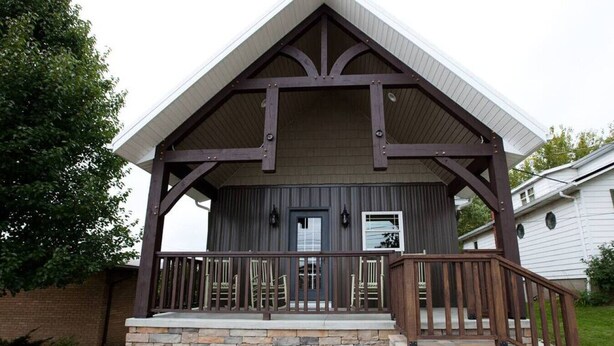 Un bâtiment à deux étages, doté de fondations en pierre et d’un porche en bois avec une balustrade.
