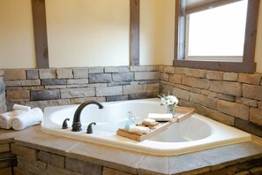 A bathroom with a stone wall, a large bathtub, and a wooden tray with toiletries.
