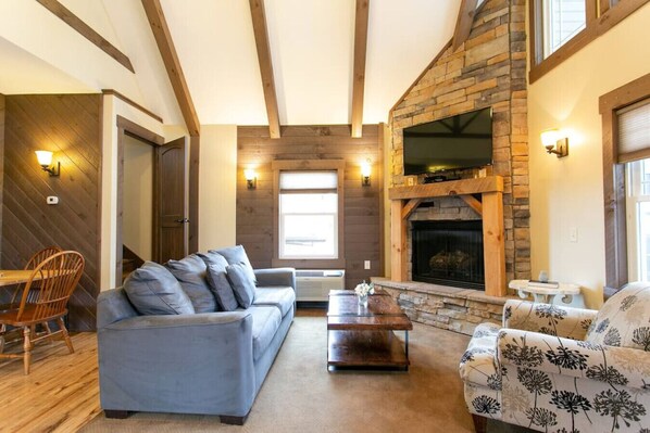 A cozy living room with a stone fireplace, wooden beams, and a large sofa.