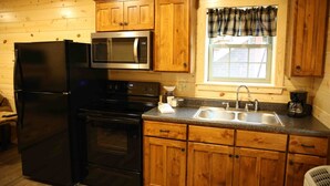 Cocina con gabinetes de madera, un refrigerador negro, microondas, estufa y lavaplatos.