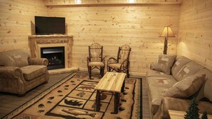 Acogedor interior de cabaña de troncos con chimenea, sofás de cuero, sillas de madera, un televisor y una alfombra estampada.