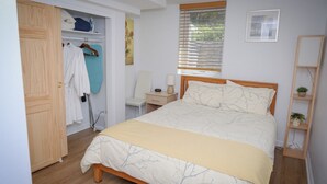 A bedroom with a bed, a wardrobe, a chair, a bedside table, and a window with blinds.