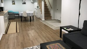 A modern living room with a sofa, a dining area with a table and chairs, a kitchen area, and a staircase leading to another level.