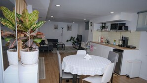 A modern kitchen with a microwave, coffee maker, and a small refrigerator. There is a dining area with a table and chairs, and a large potted plant.