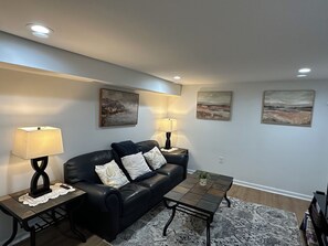 A living room with a black leather sofa, two side tables with lamps, and two wall-mounted paintings. - One bedroom w Private Entrance close to DC (Silver Spring)