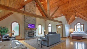 Un loft spacieux avec une cheminée en pierre, un grand salon doté d’un canapé et d’une télévision, une chambre séparée avec un grand lit et un jacuzzi dans un coin.