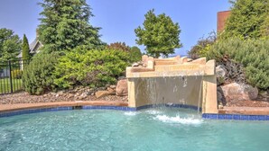 Une piscine agrémentée d’une cascade, entourée de rochers et d’arbres.