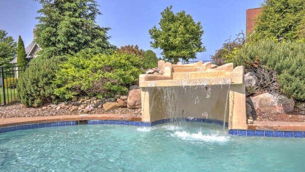 A clear pool with a waterfall feature, surrounded by rocks and greenery.