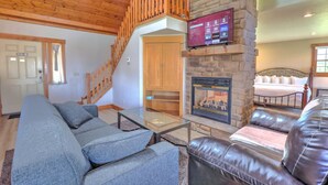 A living room with a stone fireplace, a television mounted above it, a sofa, a leather couch, and a staircase leading to another room.