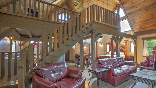 A spacious living area with leather sofas, a wooden staircase, and a high ceiling. - Amish Country Getaway With Seasonal Pool/Hot Tub (Millersburg)