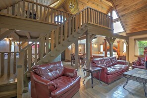 A spacious living area with leather sofas, a wooden staircase, and a high ceiling.