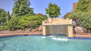 A swimming pool with a waterfall feature, surrounded by rocks and trees. - Amish Country Getaway With Seasonal Pool/Hot Tub (Millersburg)
