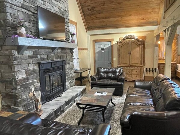 A cozy living room with a stone fireplace, leather sofas, and a wooden ceiling.