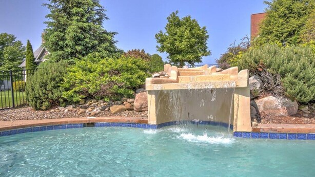 A swimming pool with a waterfall feature, surrounded by lush greenery and a stone structure. - Lovely Cottage W/ Jacuzzi & Fireplace (Millersburg)
