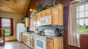 A kitchen with wooden cabinets, a stove, and a microwave. - Lovely Cottage W/ Jacuzzi & Fireplace (Millersburg)