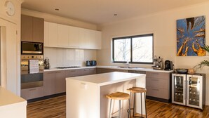 A modern kitchen with a central island, bar stools, a built-in oven, and a coffee machine.