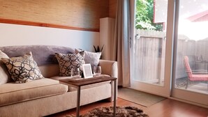 Una sala de estar con un sofá color beige, cojines estampados, una mesita de madera y un ventanal de vidrio que da a un área exterior.