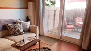 Una sala de estar con sofá, mesa de centro y puerta corrediza de vidrio que da a un patio con mobiliario exterior.