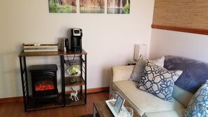 Una sala de estar acogedora con chimenea, cafetera, un florero con flores y un sofá con cojines estampados.