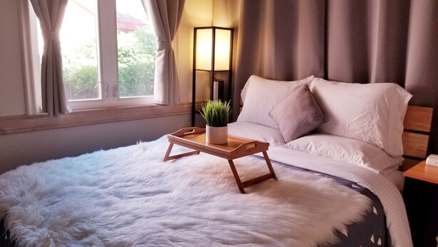 Un dormitorio con una cama grande, una mesita de noche con una lámpara y una planta, y una ventana con cortinas.