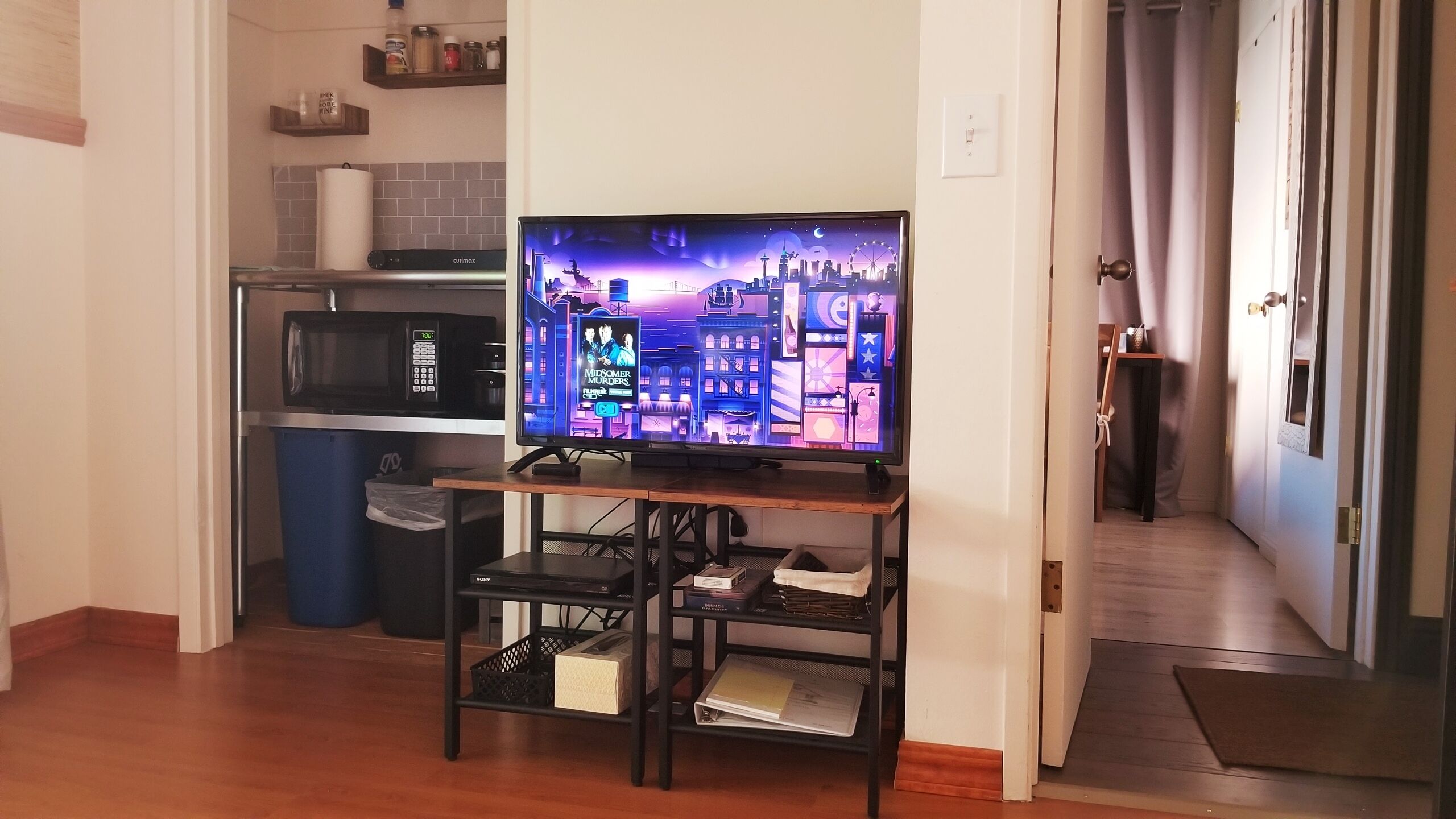 A kitchen with a microwave, a television on a stand, and a trash bin.