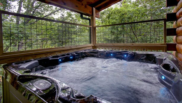 Ein Whirlpool mit Holzterrasse und Glaswänden, umgeben von Bäumen.