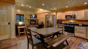 Ein Holzinnenraum mit Esstisch, Stühlen, Kamin, Fernseher und Küchengeräten.