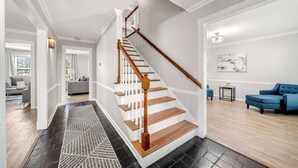 Un escalier avec des marches en bois et des rampes blanches, menant à un espace de vie agrémenté d’un canapé bleu et d’un tableau accroché au mur.