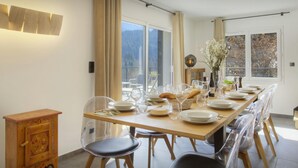A dining area with a long table set for six, clear chairs, and a small wooden cabinet. - Chalet Ysopi - modern ski base for 9 La Clusaz - OVO Network (Saint-Jean-de-Sixt)