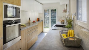 A modern kitchen with a built-in oven, a microwave, and wooden cabinets. There is a window providing natural light and a view of the outdoors. - Chalet Ysopi - modern ski base for 9 La Clusaz - OVO Network (Saint-Jean-de-Sixt)