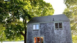 A small, single-story cabin with a shingled exterior, a visible door, and a window. - Rustic Lakeside Cabin at White Gate Farm (East Lyme)