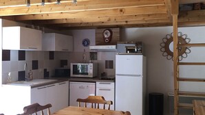 Una cocina con armarios blancos, un microondas, un refrigerador y una mesa de comedor de madera con sillas.
