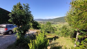 A scenic view of a rural landscape with a car parked on a gravel path, surrounded by lush greenery and hills in the background.