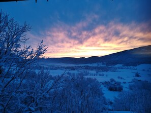 Eine verschneite Landschaft bei Sonnenuntergang, mit einem Tal und weit entfernten Hügeln.