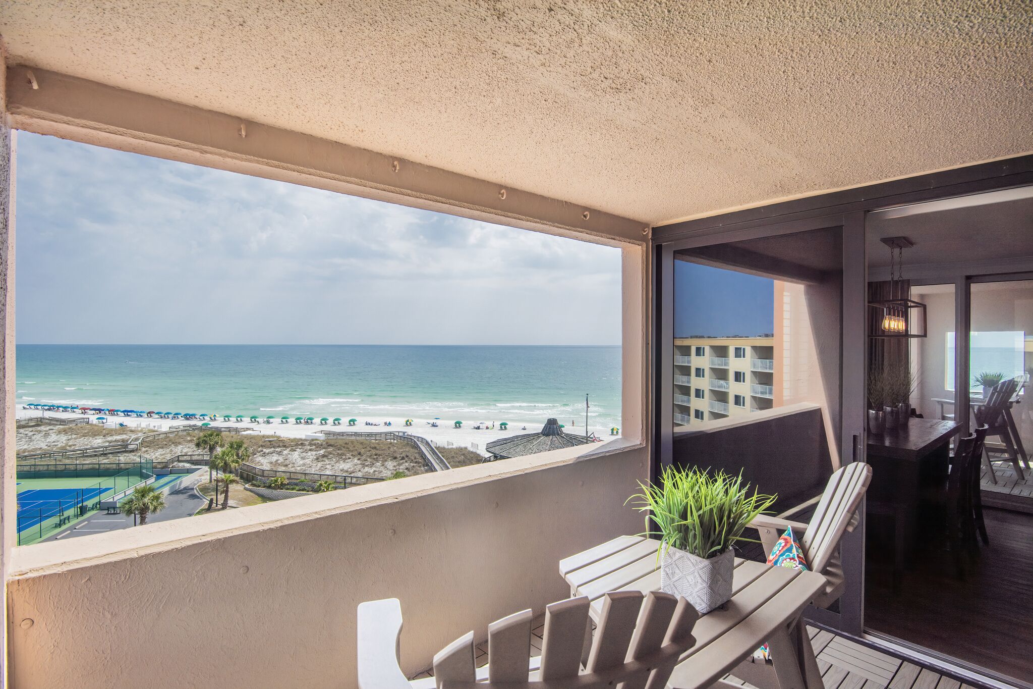 Ein Balkon mit Blick auf den Strand, eine Essecke mit Stühlen und einem Tisch sowie ein Blumentopf.