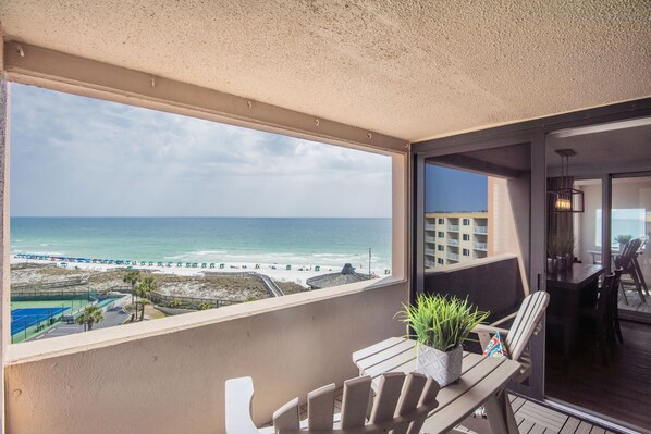 A balcony with a view of the beach, a dining area with chairs and a table, and a potted plant. - Fabulous sunset Jetty view! Enjoy one free beach chair setup each day! (Destin)
