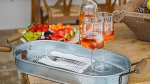 Een eettafel met een champagnefles, twee glazen, een fruitschaal en een metalen dienblad met bestek.