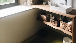 Ein Badezimmer mit Steinwand, einem Fenster, einem Waschbecken und Regalen mit Körben.