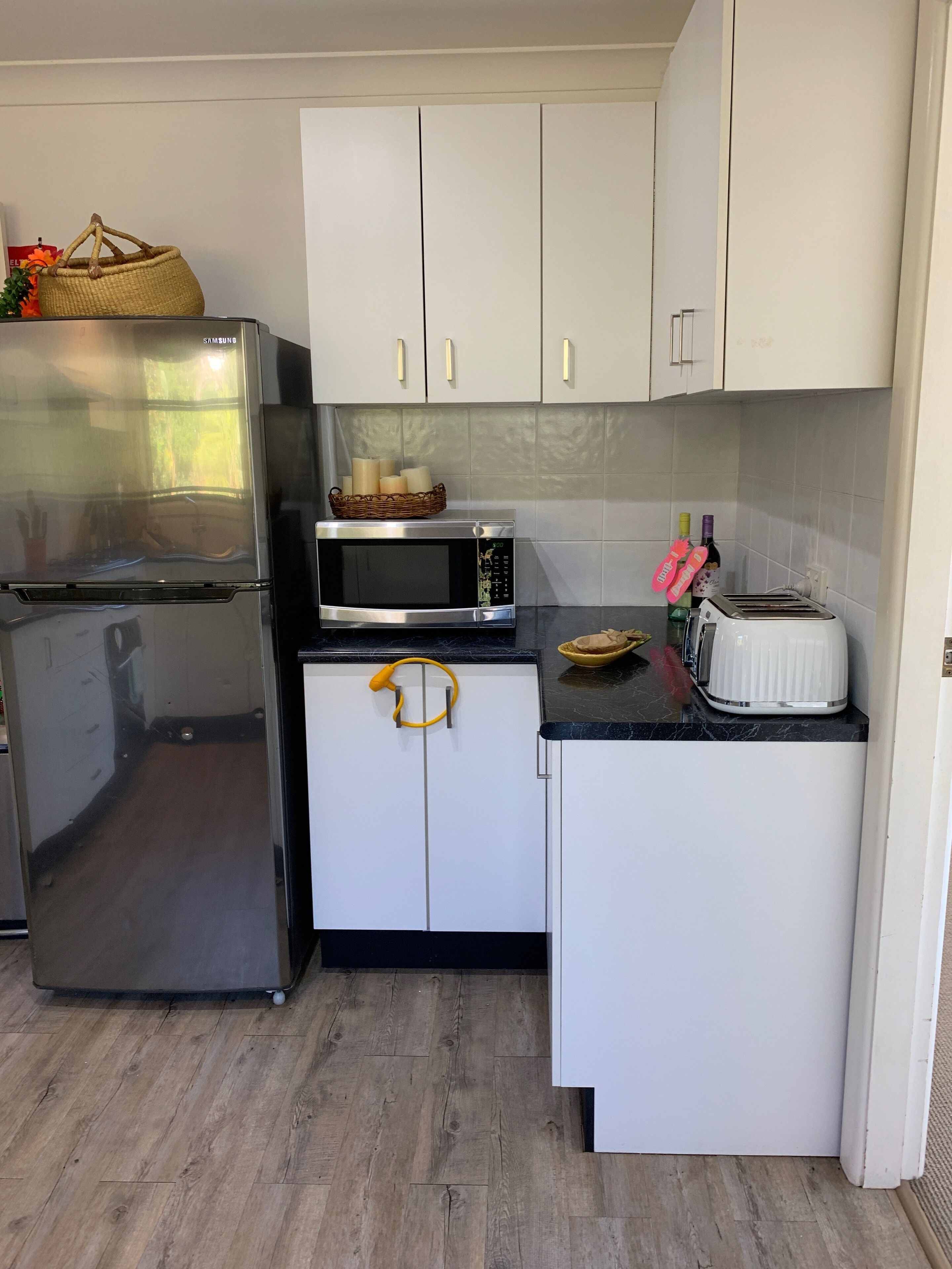 A compact kitchen with a refrigerator, microwave, toaster, and cabinets.