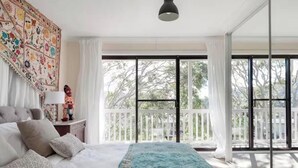 A bedroom with a large bed, a nightstand with a lamp, a colorful tapestry, and a balcony with a white railing. - Casa de Piña, 700 mts to Newport Beach, headland views, spacious 2 bedrm apt.  (Newport)