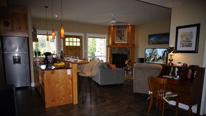 A spacious kitchen with a central island, wooden cabinets, and a built-in refrigerator. There is a dining area with a sofa and chairs, and a fireplace with a mantel. - Dreams B&B (Summerland)