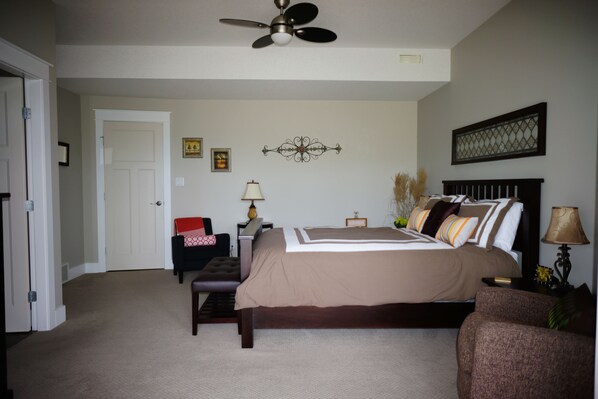 A bedroom with a bed, a desk, a chair, a bench, a ceiling fan, and a door.