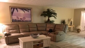 Un soggiorno con un divano angolare beige, un tavolino bianco con una ciotola, un quadro appeso al muro e una pianta di palma.