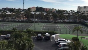 Un parcheggio con diverse automobili, un campo da tennis e edifici sullo sfondo.
