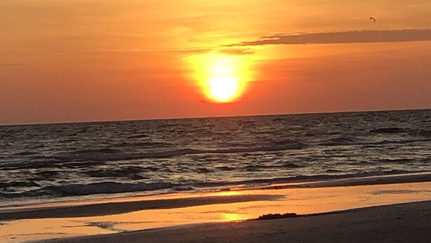 Tramonto sull'oceano con una spiaggia in primo piano.